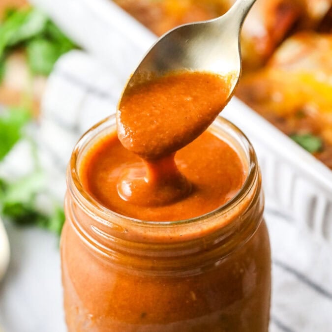 Homemade enchilada sauce being spooned from a jar.