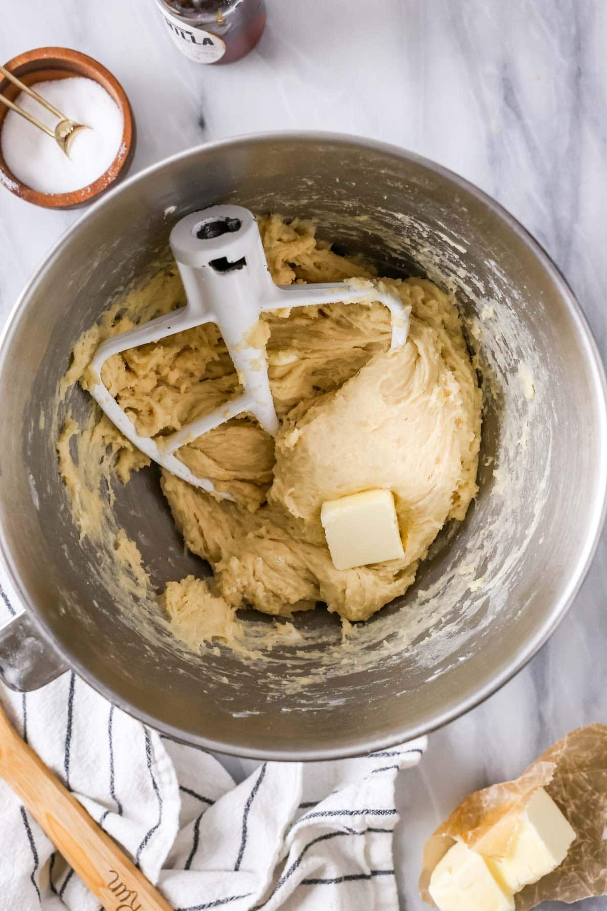 Mixing bowl with amish cinnamon roll dough and a tablespoon of butter and kitchenaid paddle attachment.