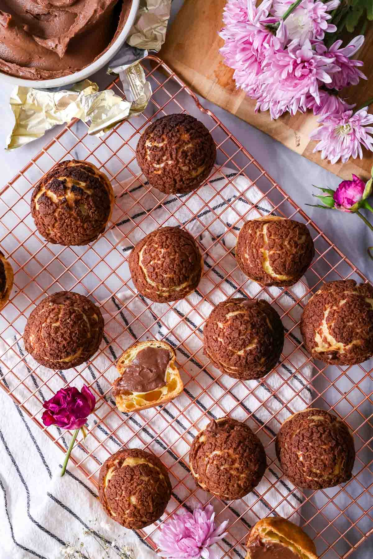 Overhead view of choux buns topped with a chocolate craquelin on a cooling rack.