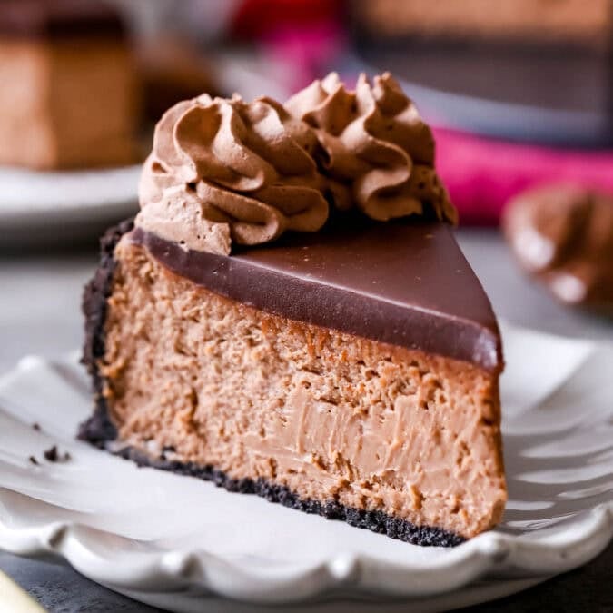 Slice of Nutella cheesecake topped with chocolate ganache and chocolate whipped cream. on a plate.