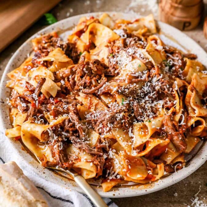 Plate of short rib ragu over pappardelle pasta topped with grated parmesan cheese.