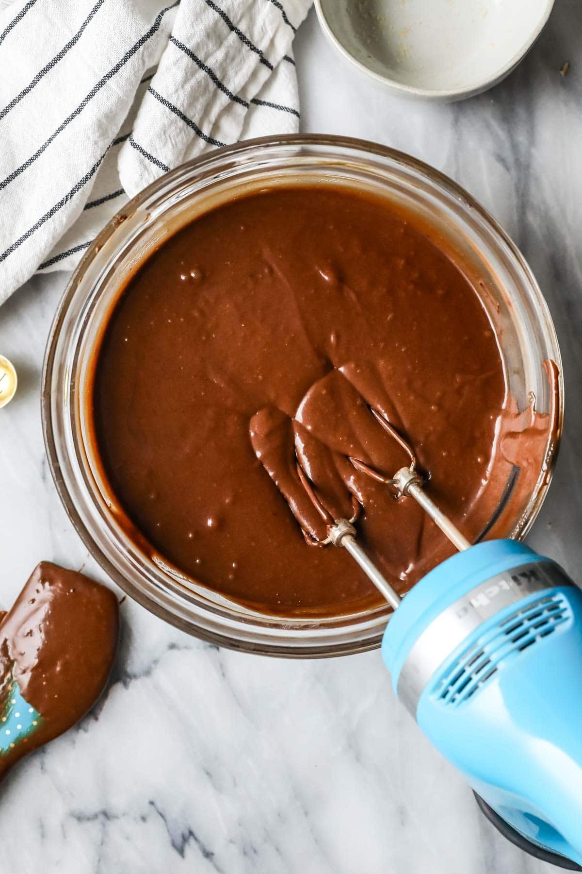 Overhead view of chocolate cake batter being mixed with a hand mixer.