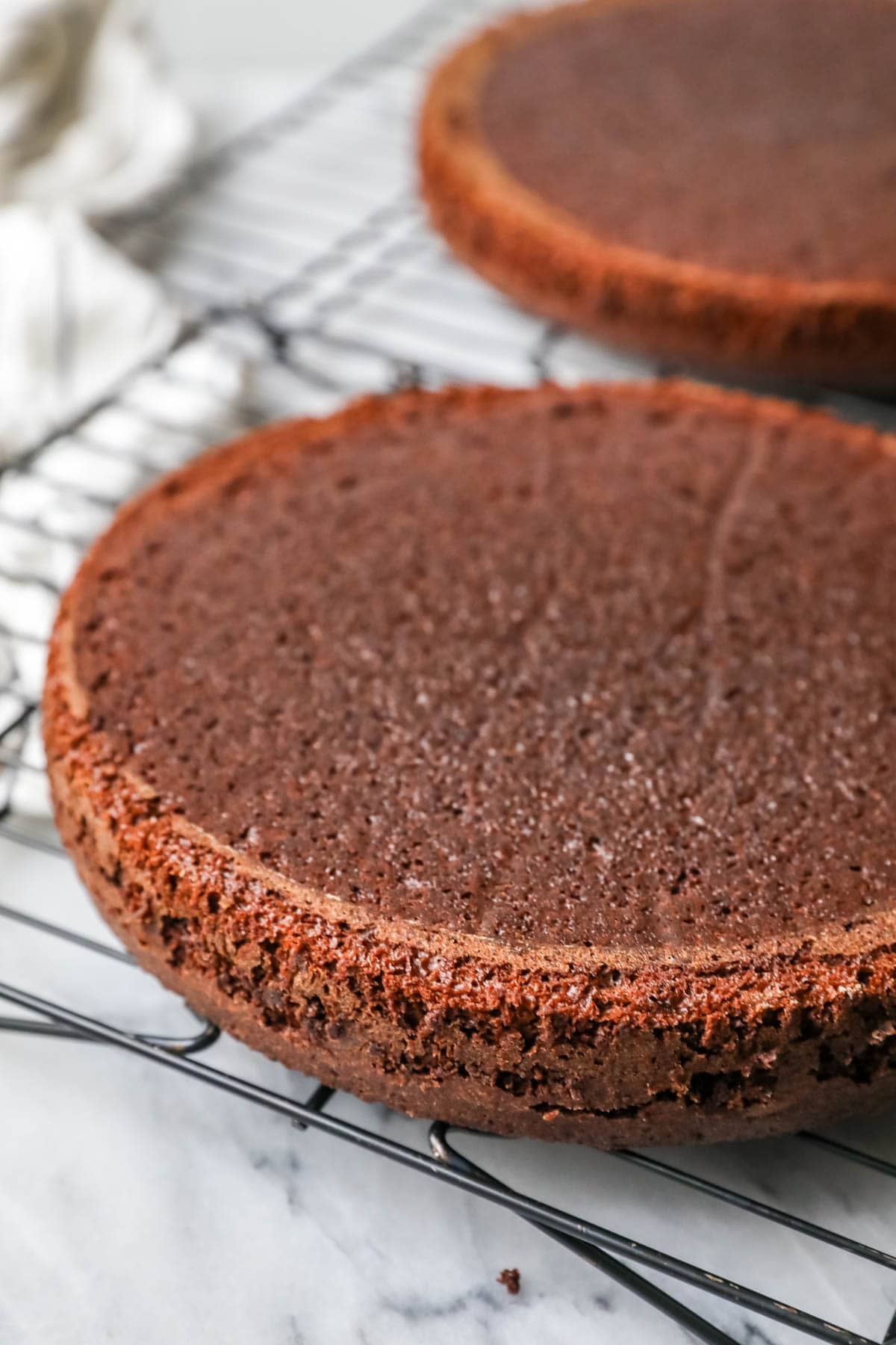 Two chocolate cake layers on a cooling rack.
