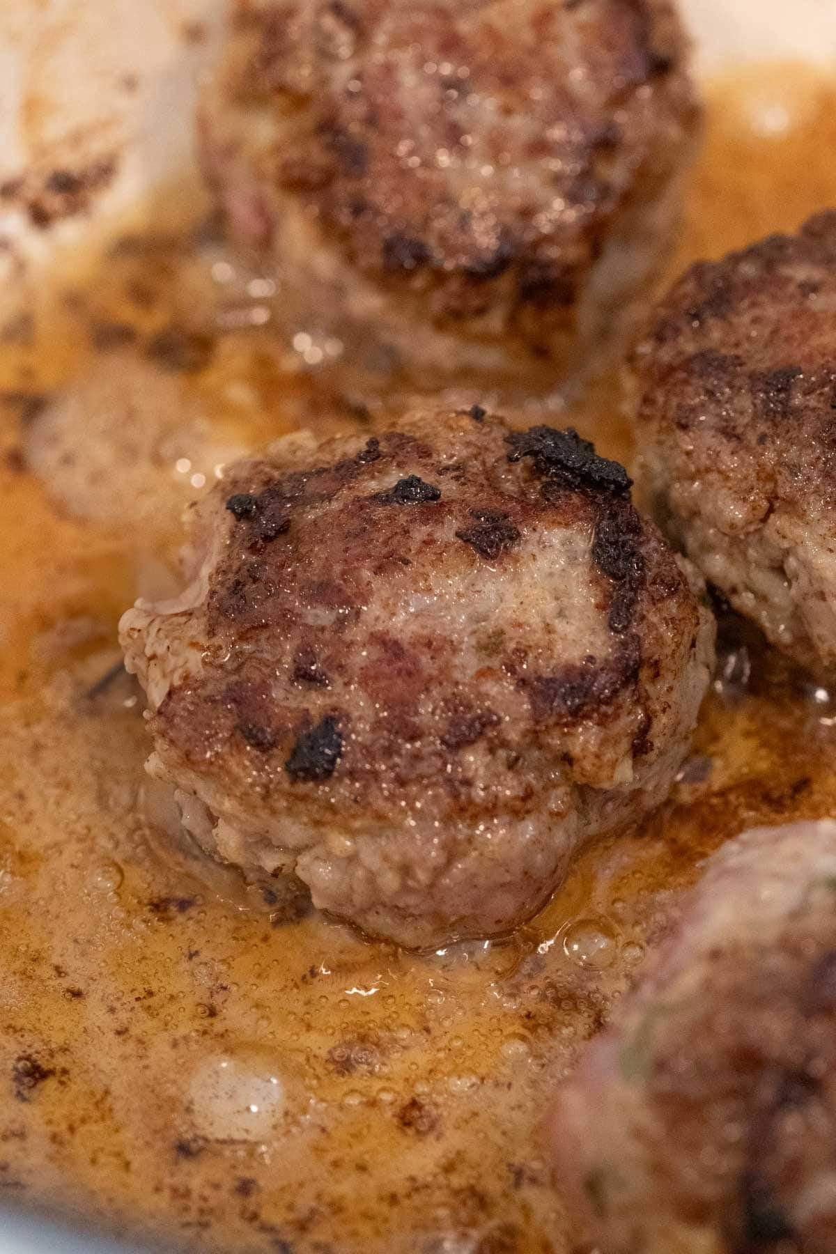 Close-up view of meatballs searing in a pan.