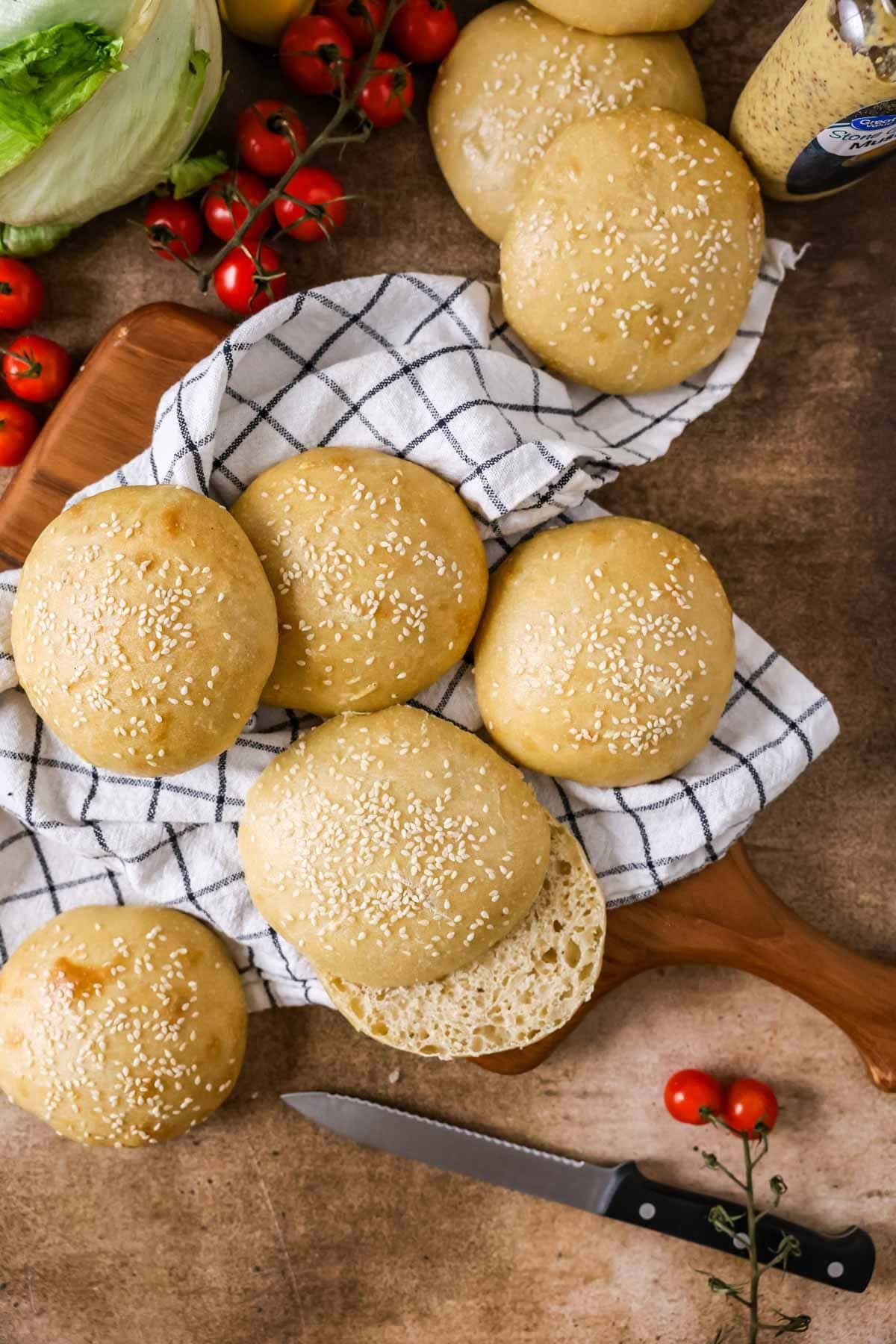 Overhead view of homemade sourdough hamburger buns topped with sesame seeds on a kitchen towel.