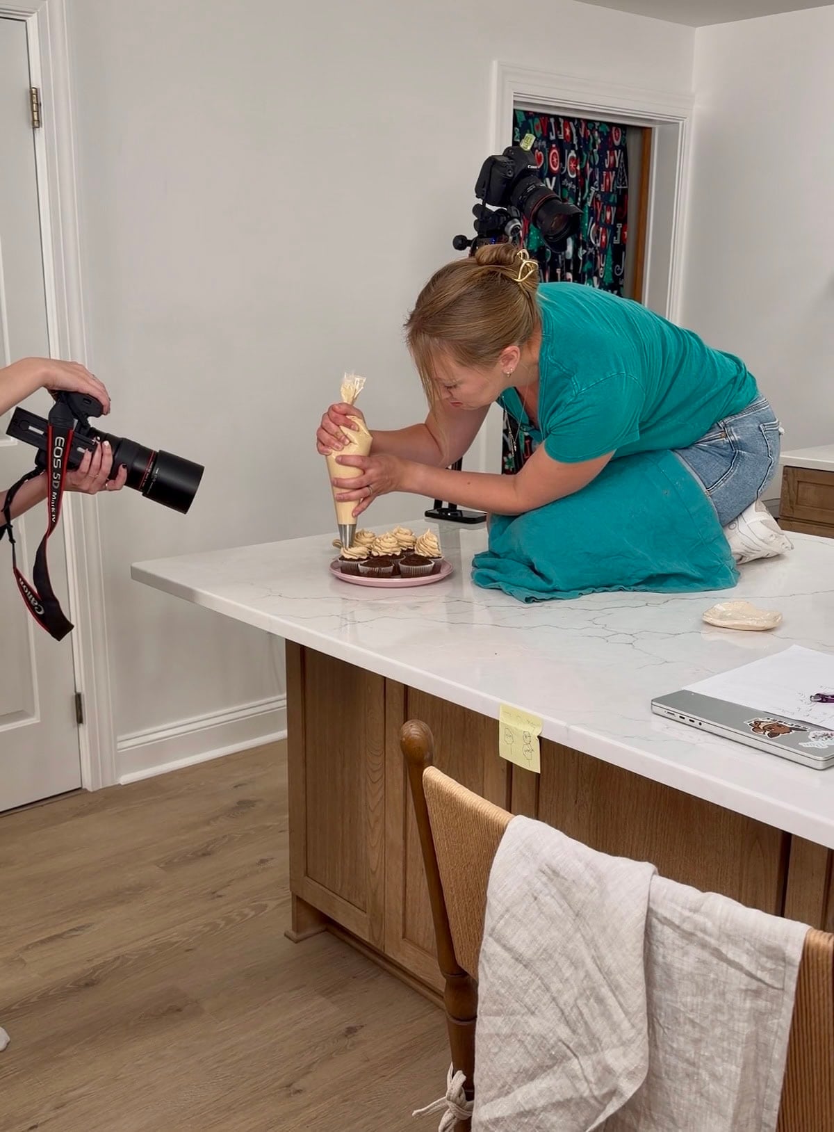 The author sitting on the counter swirling peanut butter frosting on cupcake