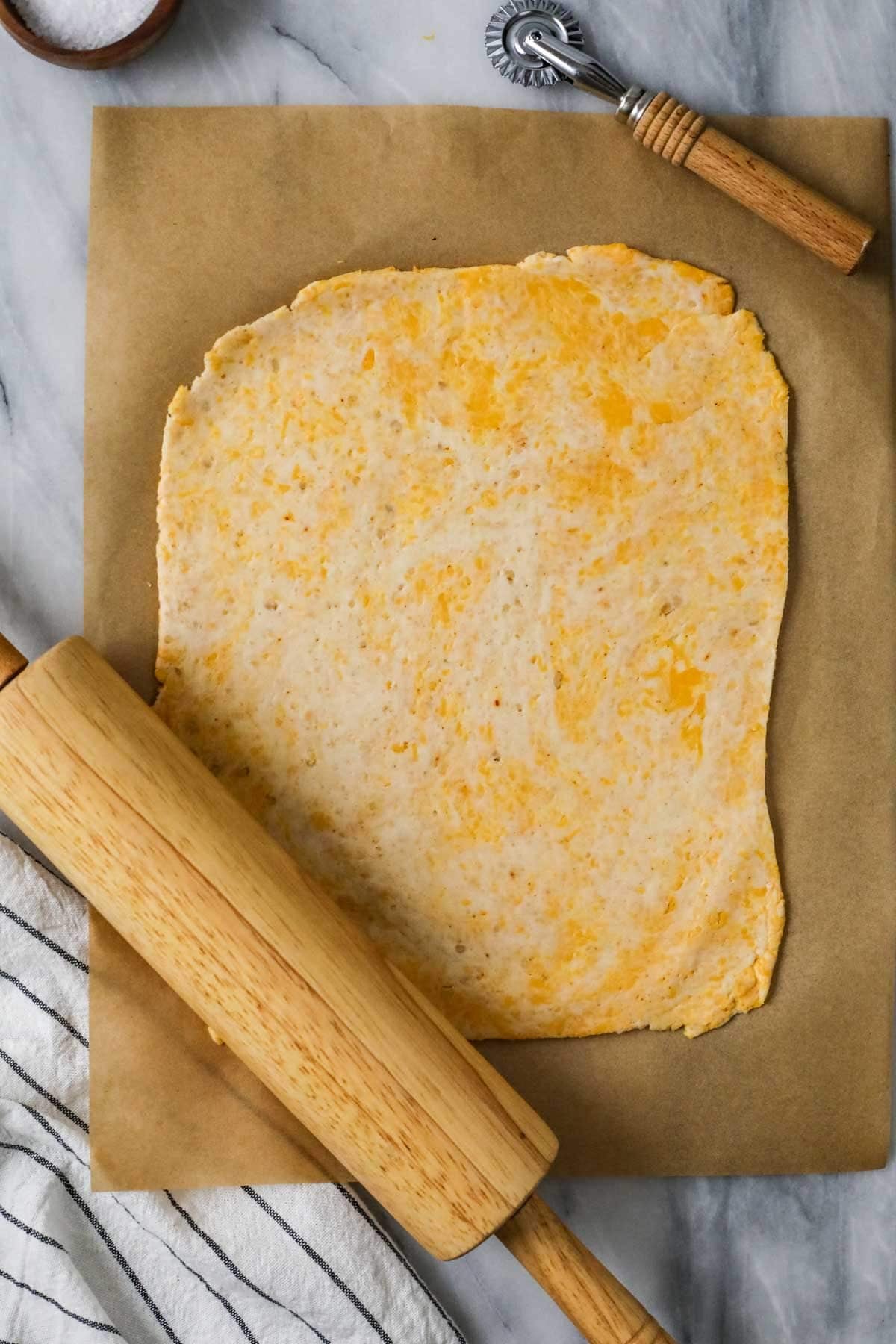 Rolling pin rolling out a thin layer of cheese-infused dough.