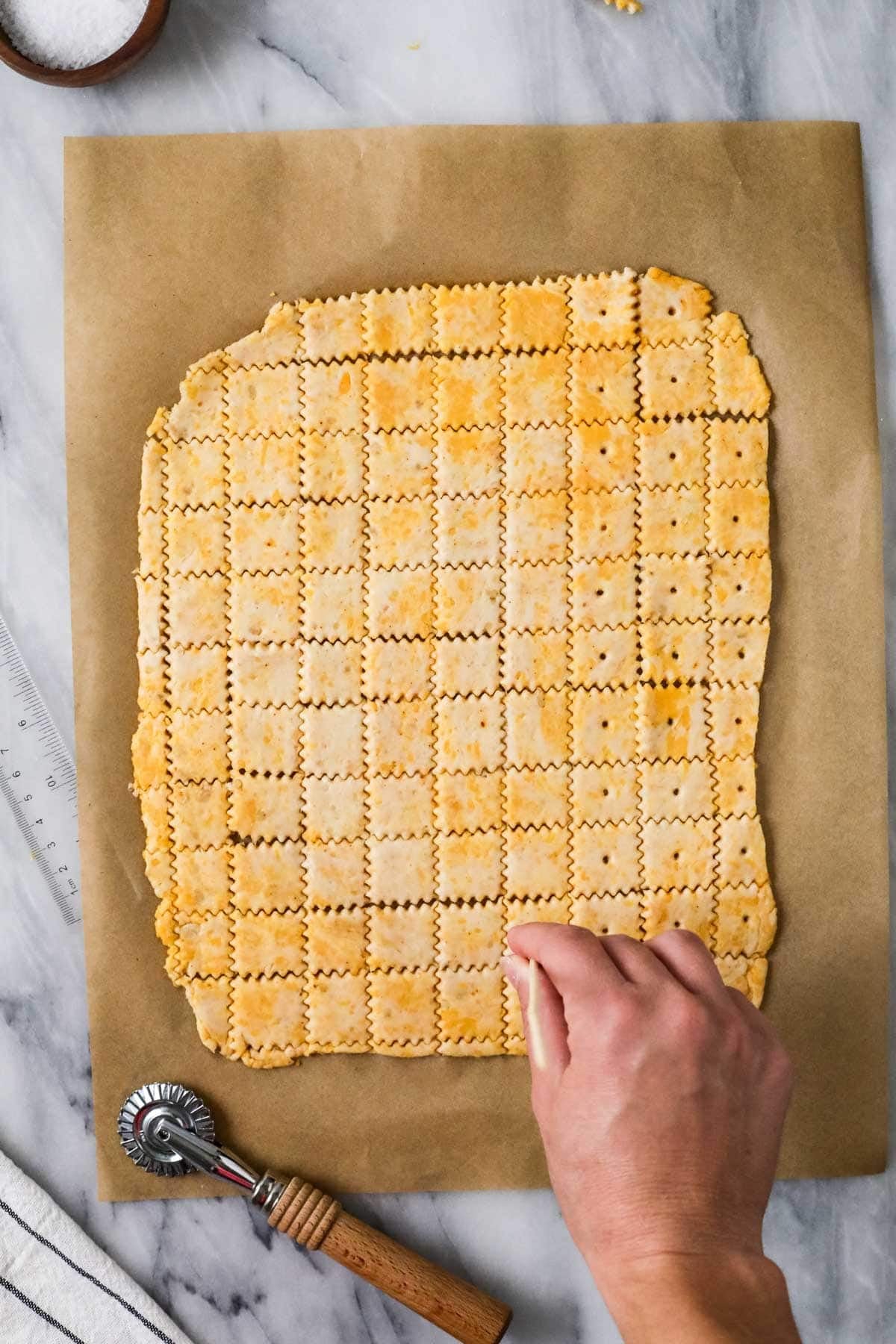 Overhead view of holes being poked into a cracker dough on a baking sheet.