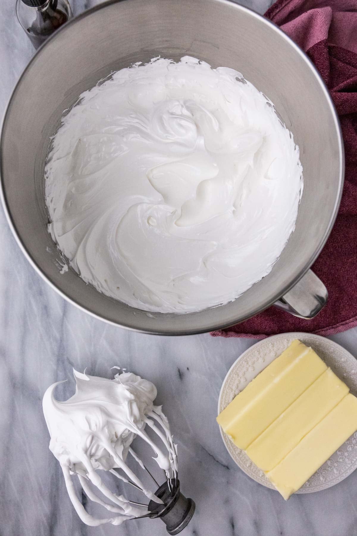 Overhead view of a bowl of fluffy meringue in a mixer bowl beside sticks of butter.